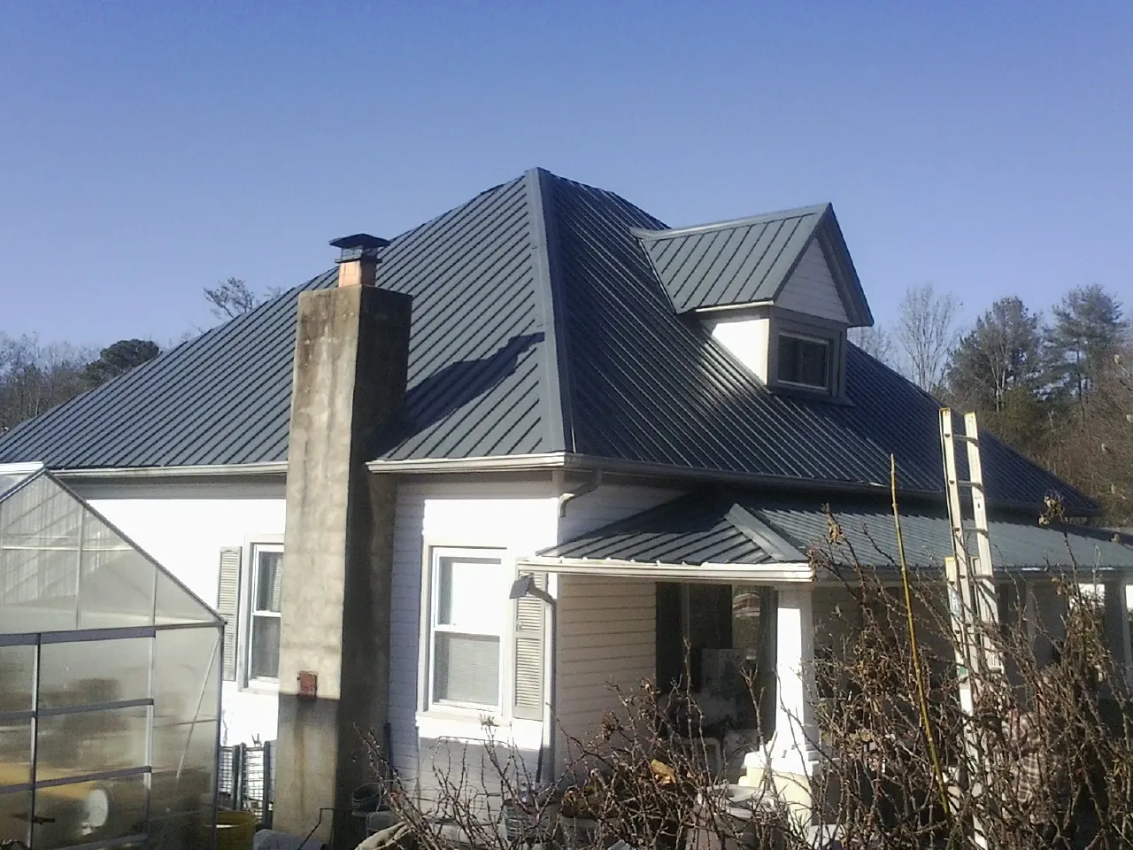 Dark blue standing seam metal roof on a white farmhouse with dormer — Slate & Tile Roof Repair by Roofing Brothers in Duck Creek Village