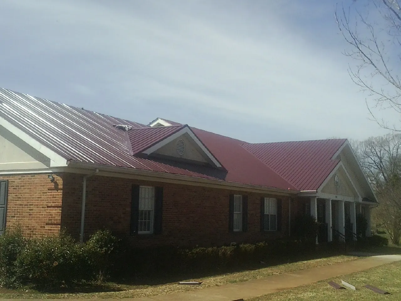 Red metal roof with gabled entries on a long brick building, from a Hail Damage Roof Repair job in Duck Creek Village