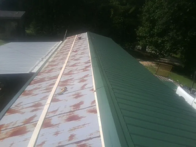 Old rusted panels beside newly installed green metal roofing — Wind Damage Roof Repair by Roofing Brothers in Duck Creek Village