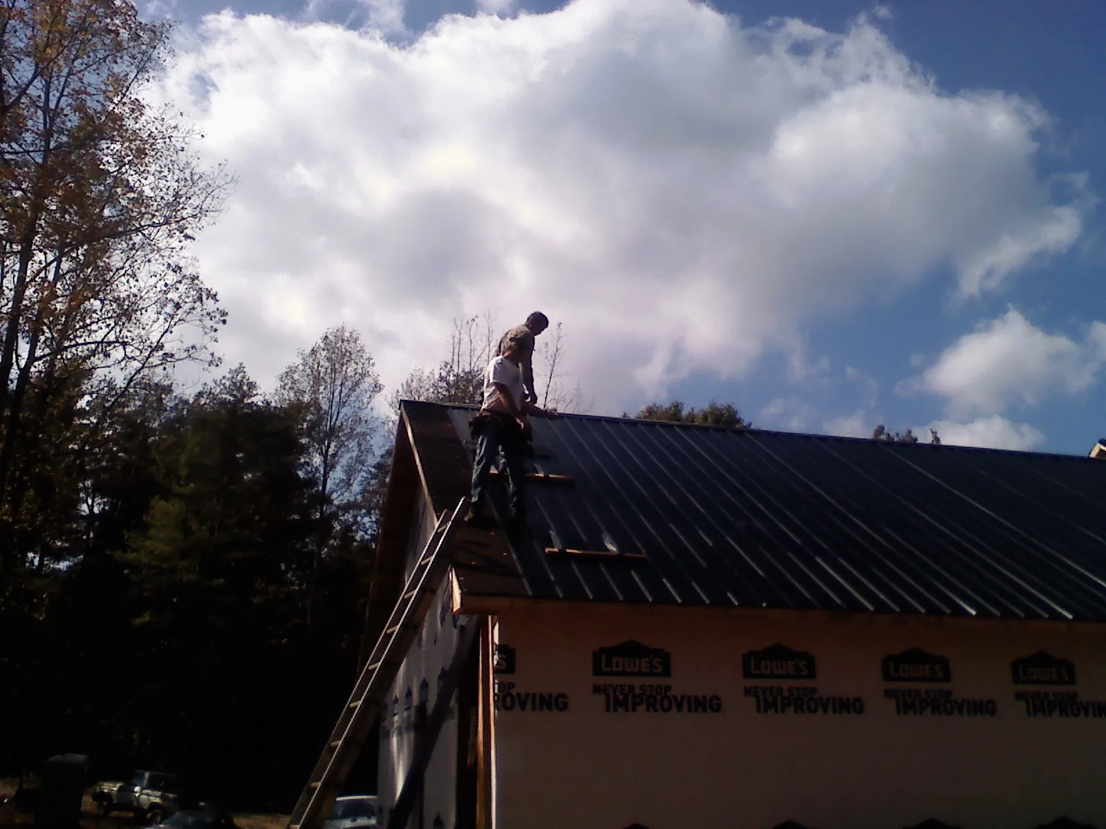 Roofer fastening dark metal panels high against a cloudy sky, from a Roof Inspection job in Duck Creek Village