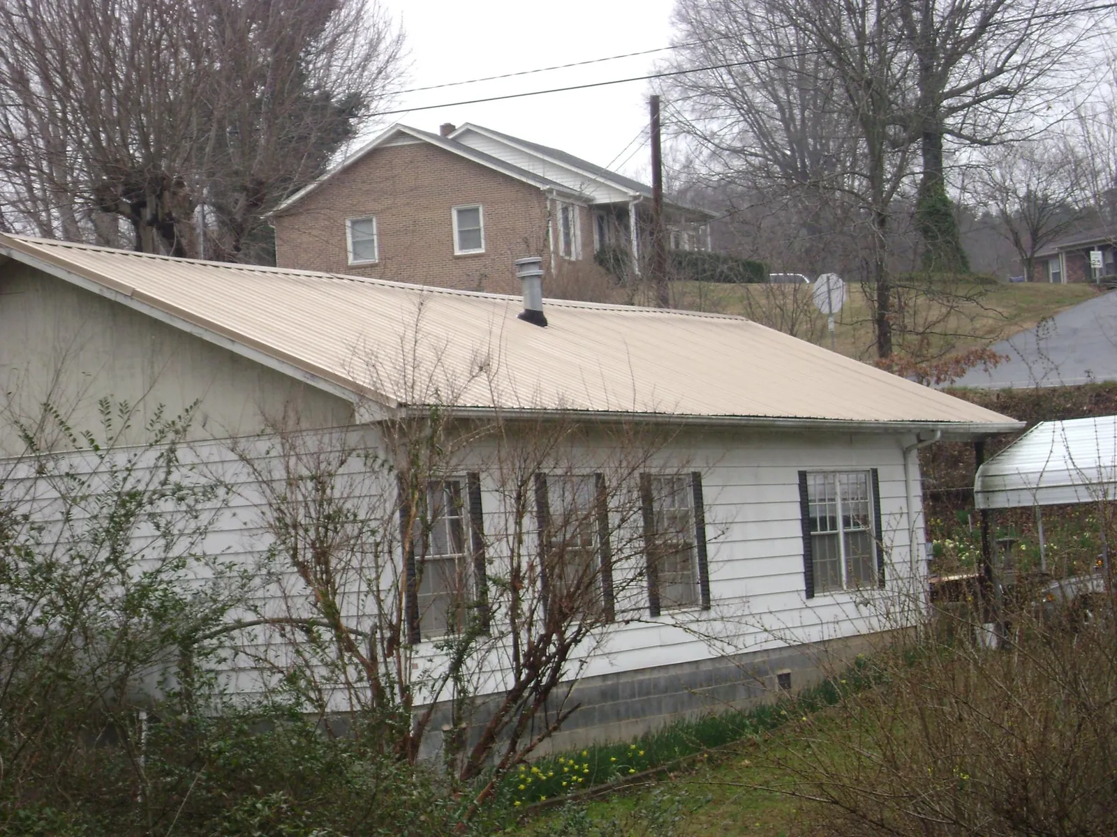 Tan metal roof on a white sided house set into a hillside — Commercial Roofing by Roofing Brothers in Duck Creek Village