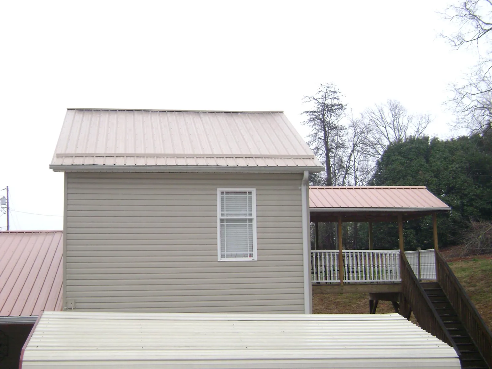 Tan metal roofs on a two story addition and attached porch, from a Roof Replacement job in Duck Creek Village
