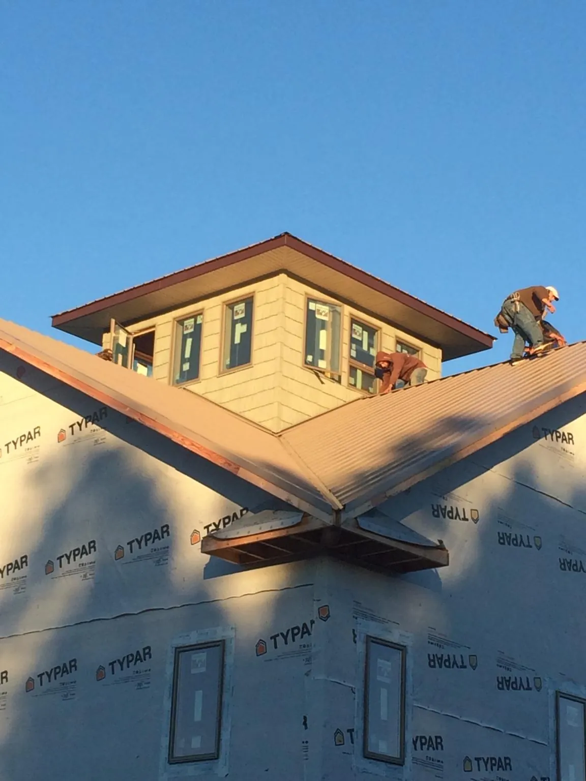 Roofers working around a rooftop cupola on a new metal roof at sunset — Roof Waterproofing in Duck Creek Village by Roofing Brothers